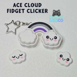 Può includere: Un clic fidget a forma di nuvola bianca con un design arcobaleno. L'arcobaleno ha strisce nere, grigie, bianche, viola e blu chiaro. Il clic è attaccato a un portachiavi a forma di stella argentata.