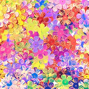 May include: A colourful collection of iridescent flower-shaped sequins in shades of yellow, pink, red, purple, and blue. These decorative embellishments have a reflective, shiny surface, ideal for craft projects and decorations.