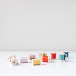 May include: Assortment of colourful thread spools in various shades of pink, red, orange, yellow, blue and white. The spools are made of wood and have metal clasps.