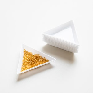 May include: Two white triangular trays, one filled with small, golden beads, the other stacked on top of itself.
