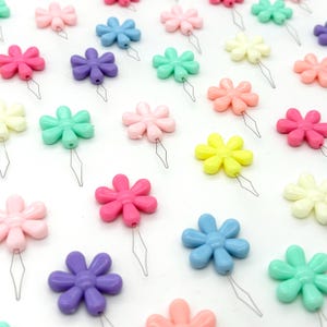 May include: Assortment of colourful flower-shaped threaders with metal needles. The threaders are in various colours, including pink, blue, green, yellow, and purple.