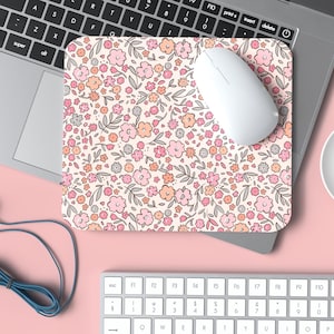 May include: A white computer mouse sits on a floral mousepad with a pink, orange, and gray pattern. The mousepad is on a pink surface.
