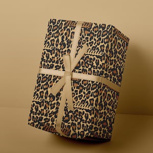 May include: A gift box wrapped in leopard print wrapping paper with a gold ribbon. The wrapping paper has the name "Natalie" printed on it.