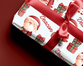May include: White gift wrap with a red ribbon and a repeating pattern of Santa Claus illustrations, presents, and the word "Deacon".