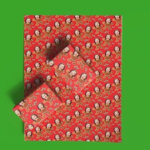 May include: Red wrapping paper and gift boxes with a repeating pattern of gingerbread people with a woman's face. The gingerbread people are brown with white icing details. The background is red.
