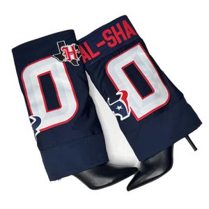 May include: A pair of black heeled boots with a navy blue jersey fabric covering the top of the boot. The jersey fabric has a white number "00" with red trim and a red and white Houston Astros logo.