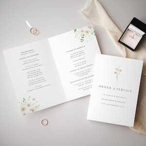 May include: A wedding ceremony order of service with white daisies and greenery. The text reads "Order of Service" with the names "Victoria & Michael" and the date "20th September 2010".