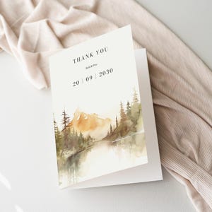 Puede incluir: Una tarjeta de agradecimiento blanca con una ilustración de acuarela de una cordillera, un lago y árboles. El texto "THANK YOU" está impreso en negro en la parte superior de la tarjeta, seguido de "Beth & Peter" y la fecha "20 | 09 | 2030".