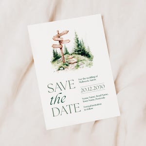 May include: A cream-colored wedding invitation with a watercolor illustration of a wooden signpost in a forest. The text "SAVE the DATE" is in green, along with the wedding date and names.