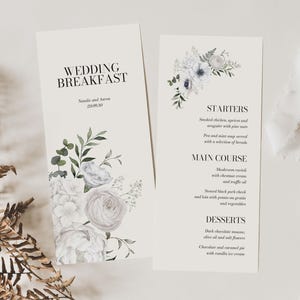May include: Wedding breakfast menu featuring a floral design with white flowers and green leaves. The menu includes starters, main course, and desserts.
