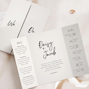 Op de afbeelding: Elegante witte trouwuitnodiging met zwarte kalligrafie. De uitnodiging toont de namen "Daisy + Jacob" en evenementdetails. Bevat een tijdlijn, details en RSVP-informatie. Twee gouden trouwringen zijn zichtbaar.