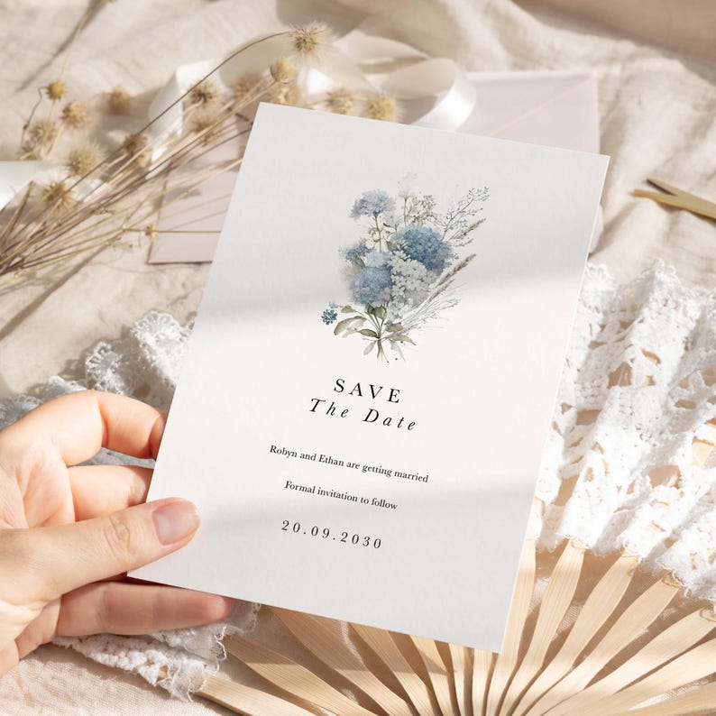 May include: A white Save the Date card featuring a watercolor illustration of blue and white flowers. The text reads: SAVE The Date, Robyn and Ethan are getting married, Formal invitation to follow, and the date 20.09.2030 in black serif font.