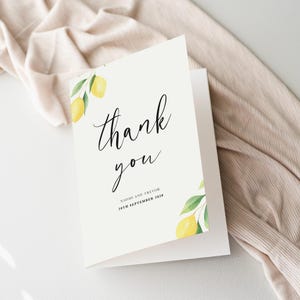 Puede incluir: Una tarjeta de agradecimiento blanca con un diseño de limón y hojas. El texto de la tarjeta dice "gracias" en letra cursiva negra. Debajo del texto está el nombre "Naomi y Trevor" y la fecha "28 de septiembre de 2020".