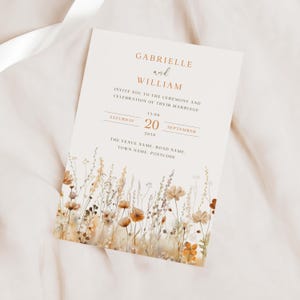 May include: Wedding invitation with a floral design in shades of brown, beige, and white. The invitation reads "Gabrielle and William invite you to the ceremony and celebration of their marriage. Saturday, September 20, 2030, 1:00 PM. The Venue Name, Road Name, Town Name, Postcode."