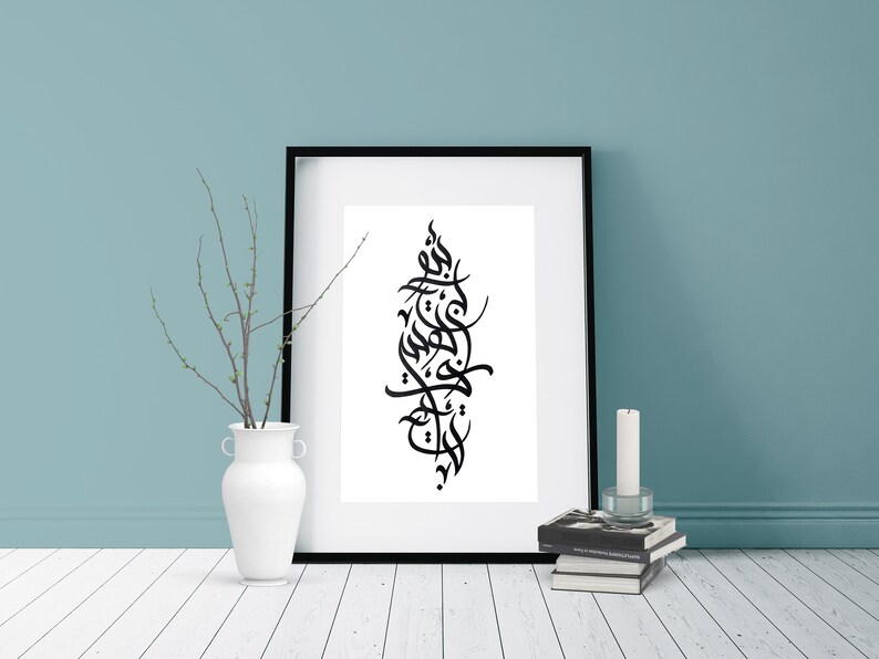 May include: A black and white calligraphy print in a black frame, hanging on a light blue wall. The print features Arabic script in a vertical design.