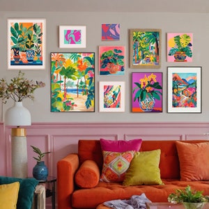 Puede incluir: Una sala de estar con un sofá naranja, un puf rosa y una mesa de centro de vidrio. Las paredes están pintadas de rosa y decoradas con obras de arte enmarcadas que representan plantas tropicales, flores y paisajes.