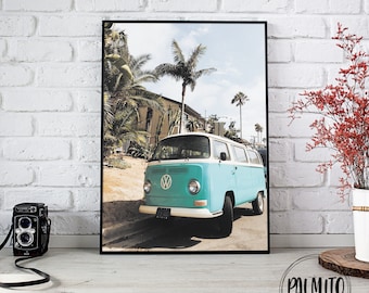May include: A vintage teal blue Volkswagen van parked on a street with palm trees and a blue sky. The van has a white roof and a white VW logo on the front.