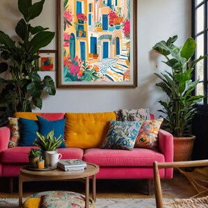 May include: A colorful painting of a narrow street in a Mediterranean village. The buildings are painted in shades of yellow and white, with blue doors and windows. There are potted plants and flowers on the balconies and in the street. The painting is framed in a gold frame and is hanging on a wall in a living room.
