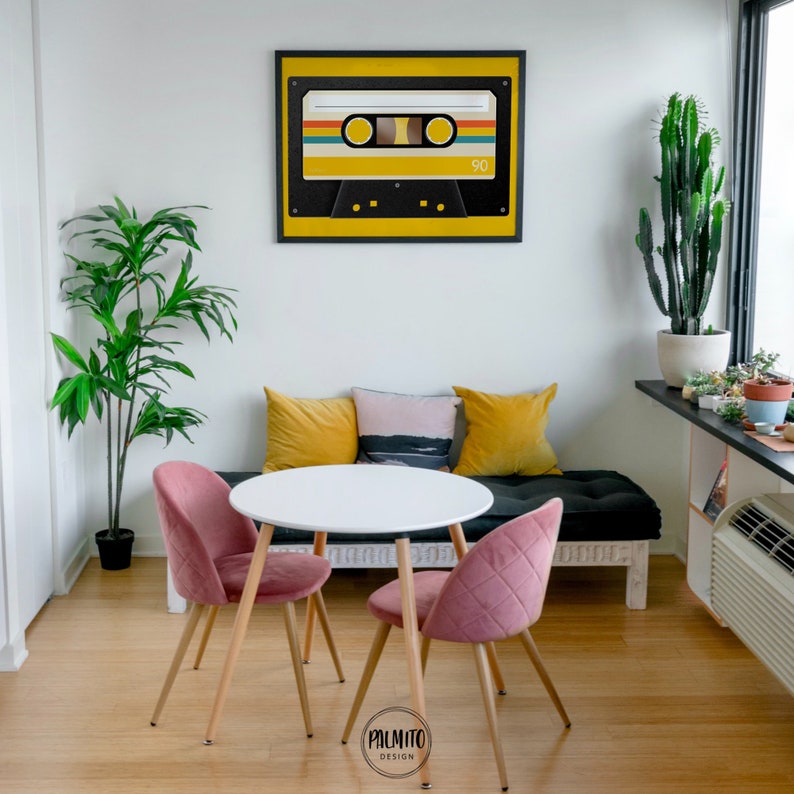 Peut inclure: Une table ronde blanche avec deux chaises en velours rose et un banc noir avec des coussins jaunes et roses. Un imprim&eacute; encadr&eacute; d'une cassette jaune avec le texte "90" dessus est accroch&eacute; au mur.