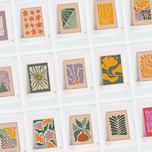 May include: A collection of framed art prints featuring abstract floral and botanical designs. The prints showcase various color palettes, including orange, green, purple, and yellow, with a neutral background. The art style is modern and minimalist.