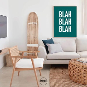 Peut inclure: Une impression encadr&eacute;e vert sarcelle avec le texte "Blah Blah Blah" en lettres blanches. L'impression est accroch&eacute;e &agrave; un mur blanc au-dessus d'un canap&eacute; blanc avec un coussin bleu. Une chaise en bois avec un coussin blanc est au premier plan.