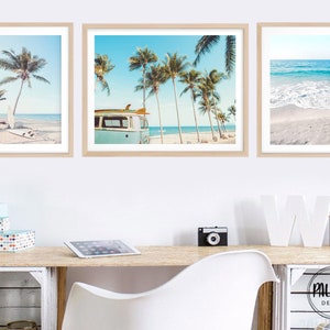Puede incluir: Tres impresiones enmarcadas de escenas de playa. La impresión de la izquierda muestra una tabla de surf en una playa de arena con palmeras en el fondo. La impresión del medio muestra una camioneta vintage estacionada en una playa con palmeras en el fondo. La impresión de la derecha muestra una playa con olas rompiendo en la orilla.