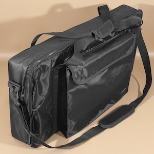 May include: Black padded bag with a shoulder strap and a zippered pocket on the front. The bag has a handle on the top and a zippered closure.