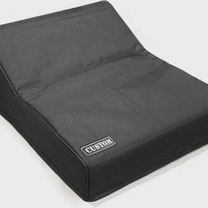 Könnte beinhalten: Eine schwarze, abgewinkelte Lautsprecherabdeckung mit rechteckiger Form. Die Abdeckung hat einen genähten Rand und einen kleinen, rechteckigen Aufnäher mit der Aufschrift "CUSTOM" in weißen Buchstaben.