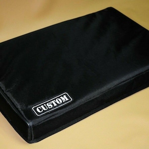 May include: A black rectangular cover with the word "CUSTOM" in a white rectangular box. The cover appears to be made of a smooth, possibly water-resistant material. The item is likely a protective case or cover.