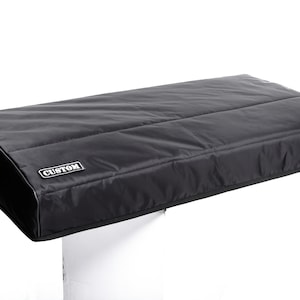May include: Black keyboard cover with a white "CUSTOM" label. The cover is made of a quilted fabric and is designed to protect a keyboard from dust and spills.