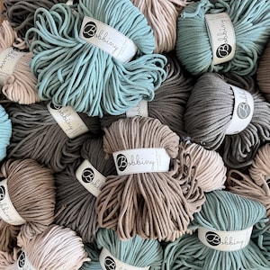 Può includere: Primo piano di una varietà di corda di cotone in diversi colori, tra cui beige, grigio e verde acqua. La corda è disposta in un mucchio e ha la parola "Bobbiny" stampata sulle etichette.