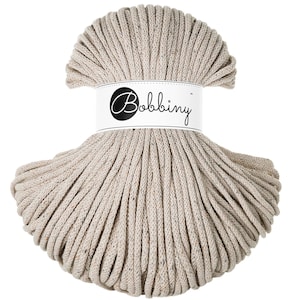 May include: A beige cotton rope, wound into a circle, with a white label that reads "Bobbiny" in black lettering.
