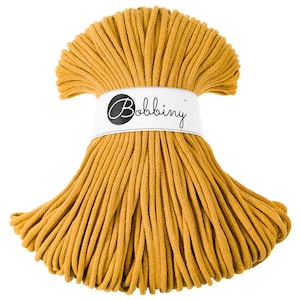 Può includere: Matassa di corda macramè color senape con un'etichetta bianca con la scritta "Bobbiny". La corda è ben avvolta e pronta per progetti di artigianato. Il colore è una tonalità calda e terrosa, perfetta per vari progetti fai-da-te.