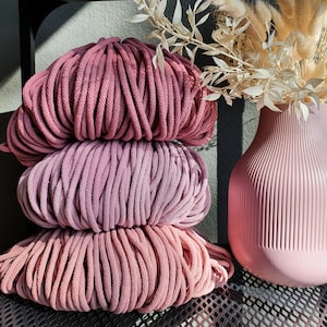Può includere: Tre bobine di corda di cotone rosa e viola impilate l'una sull'altra. La corda è morbida e testurizzata, e i colori sono tenui e rilassanti.