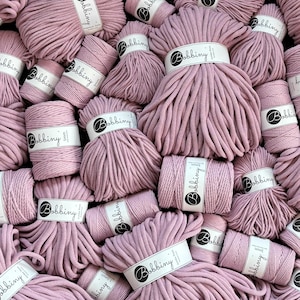 Puede incluir: Una colección de bobinas de cordón de algodón rosa polvoriento para manualidades, cada una envuelta con una etiqueta de papel blanco con la marca Bobbiny. Los cordones varían en grosor, con etiquetas que indican 3mm, 5mm y jumbo.