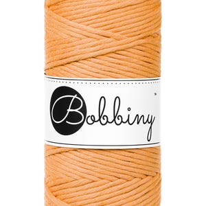 Può includere: Un rocchetto di cordoncino di cotone arancione con il nome del marchio "Bobbiny" stampato su un'etichetta bianca.