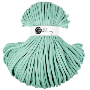 Può includere: Un gomitolo di cordoncino macramè verde menta con un'etichetta bianca con la scritta "Bobbiny". Il cordoncino è ben avvolto e pronto per progetti di artigianato. Il colore è un verde tenue e smorzato.