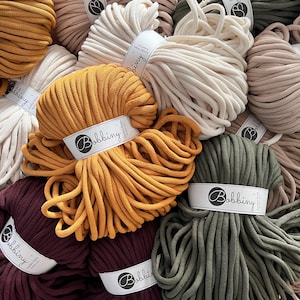 Könnte beinhalten: Eine Auswahl an bunten Baumwollseilen, perfekt für Makramee-Projekte. Das Seil ist kreisförmig angeordnet, jede Farbe in einem eigenen Abschnitt. Das Seil ist mit dem Markennamen "Bobbiny" gekennzeichnet.