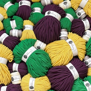 Peut inclure: Une collection de bobines de cordon en coton Bobbiny dans des tons violet foncé, vert vif et jaune moutarde. Chaque bobine est entourée d'une bande de papier blanc avec le logo Bobbiny. Les cordons sont épais, tressés et entassés.