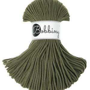 May include: A spool of olive green cotton cord, wrapped in a circle, with a white label that says "Bobbiny".