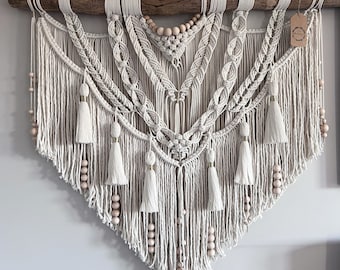 May include: A large, white macrame wall hanging with a wooden branch at the top. The macrame features a geometric design with tassels and wooden beads.
