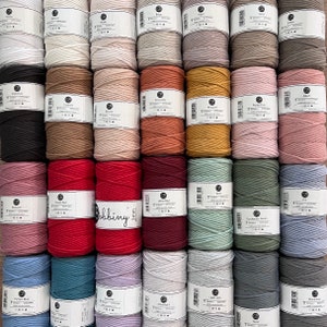 Op de afbeelding: Een assortiment van 3 mm katoenen koorden in verschillende kleuren, waaronder wit, beige, bruin, rood, roze, groen, blauw en grijs. Elke spoel is gelabeld met de kleurnaam en het merk "Bobbiny".