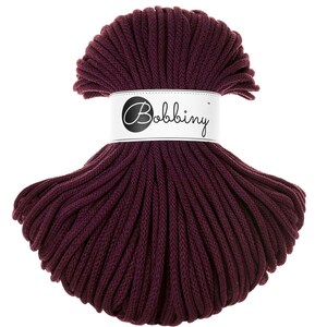 Può includere: Un grande rotolo di cordoncino di cotone color bordeaux scuro, etichettato "Bobbiny".