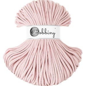 Pode incluir: Um cordão de algodão rosa, enrolado em um círculo, com um rótulo branco que diz "Bobbiny" em letras pretas.