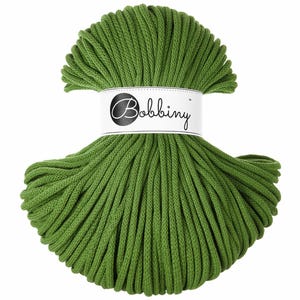 Pode incluir: Uma bola de fio verde para macramé com uma etiqueta branca com o nome "Bobbiny". O fio é de um tom verde vibrante, e a etiqueta está enrolada ao redor do centro da bola. O fio parece ser feito de um material macio e durável.