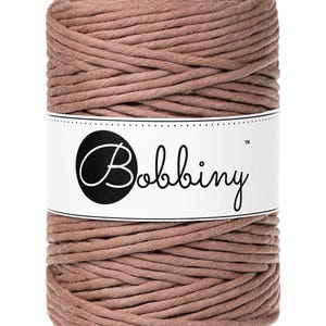 Może przedstawiać: Szpula brązowego sznurka bawełnianego z etykietą "Bobbiny" na niej.