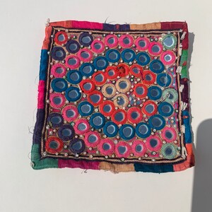 May include: A square, multi-colored fabric patch with a circular pattern of small, round mirrors surrounded by colorful embroidery.