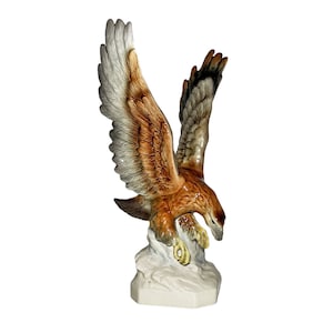 May include: A ceramic figurine of a brown and white eagle with its wings spread, perched on a white rock base.