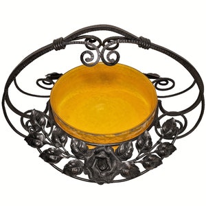 May include: A black metal bowl holder with a yellow glass bowl and a rose design. The holder has a handle and is made of wrought iron.