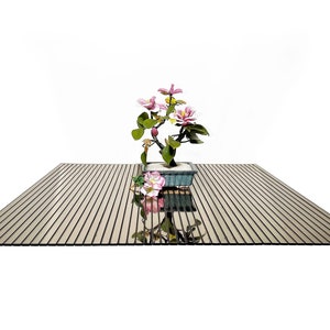 Puede incluir: Un pequeño árbol bonsái con flores rosas en una maceta azul se encuentra sobre una superficie de madera rayada.